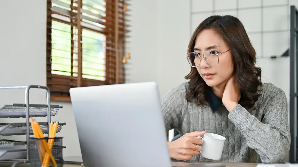 坐在辦公桌前使用筆電並手持杯子的亞洲女性