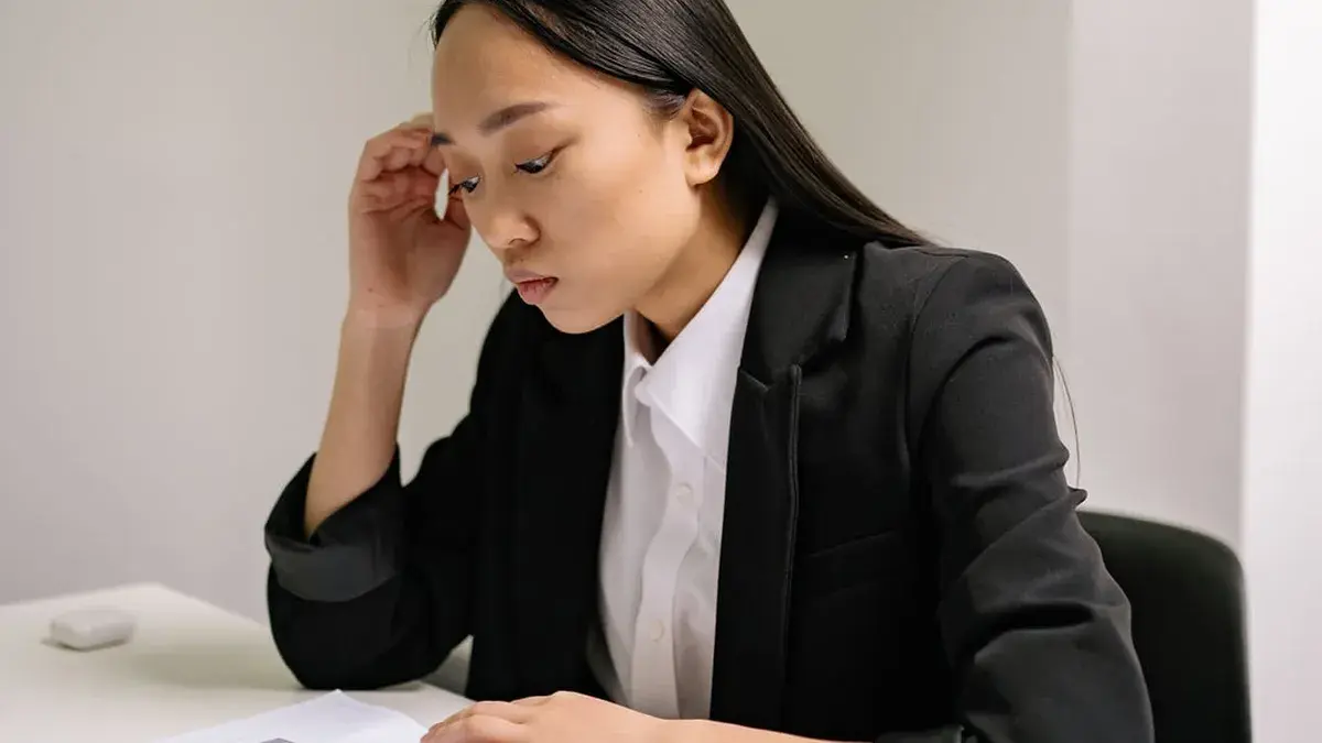 亞洲女性坐在辦公桌前閱讀資料並思考職涯困境