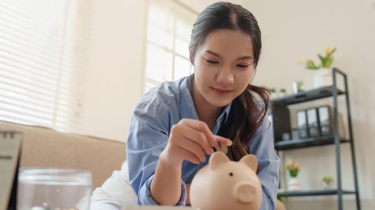 亞洲女性將硬幣投入存錢筒，規劃財富自由目標